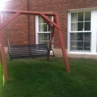 A wooden swing set on a grassy lawn in front of a brick building with windows.