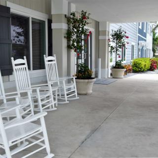 A serene porch with white rocking chairs and potted plants along a covered walkway.