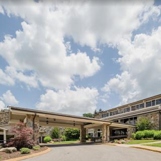 A wide-angle view of a building entrance surrounded by greenery under a partly cloudy sky.