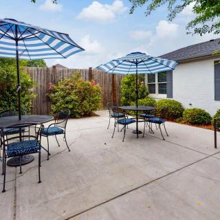 A spacious patio area with tables, chairs, and striped umbrellas surrounded by lush greenery.