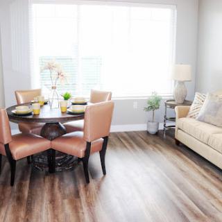 A bright and modern dining area featuring a round table with elegant chairs, complemented by a cozy sofa and natural light from large windows.