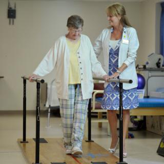 A healthcare professional assists an elderly patient during a physical therapy session focused on improving mobility.