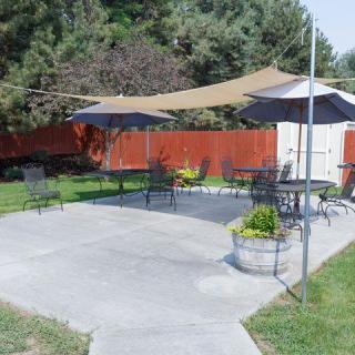 A well-furnished outdoor patio with tables and chairs, shaded by a sail canopy.