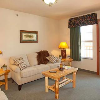 A cozy living room with a beige sofa, wooden coffee table, and lighting from an elegant lamp near the window.