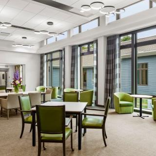 A modern dining area with green chairs, tables, and large windows allowing natural light in.