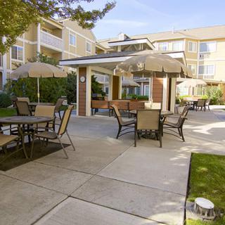 A well-maintained outdoor patio area with tables, chairs, and umbrellas at an apartment complex during the day.
