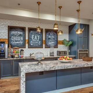 A modern kitchen with a marble island, pendant lighting, and decorative wall signs.