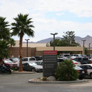 A hospital with a busy parking lot, surrounded by palm trees and mountains in the background.