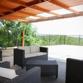A stylish outdoor patio with modern furniture under a wooden pergola, overlooking a scenic nature view.