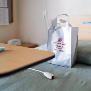 A hospital room with a bedside table and a gift bag on the bed.