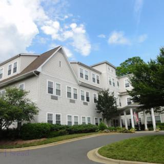 A residential building with a driveway, surrounded by trees under a cloudy sky.