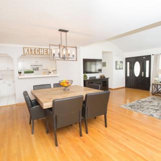 A modern dining room with a wooden table and chairs set on a polished wooden floor, leading into an open kitchen area.
