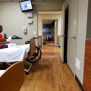 A view of a hospital patient room, featuring a wheelchair and an empty bed.