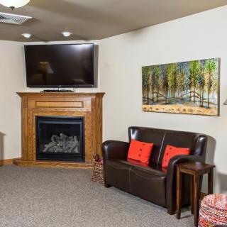 A cozy living room featuring a fireplace with a television mounted above, accompanied by a leather sofa and decorative artwork on the wall.