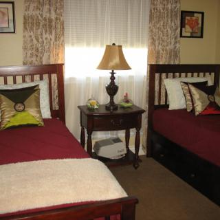 A cozy bedroom featuring two twin beds with decorative pillows, a central nightstand with a lamp, and wall art.