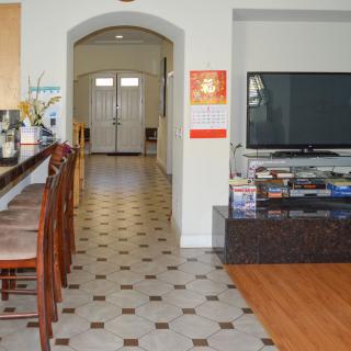 A modern kitchen with bar stools leads into a hallway, adjacent to a living area featuring a large television.