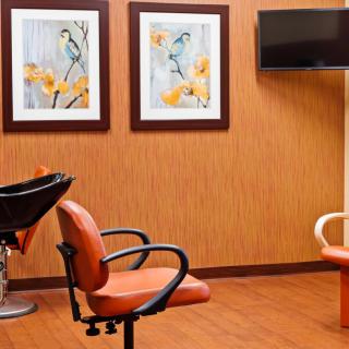 A cozy hair salon interior with modern styling chairs, decorative wall art, and a television.