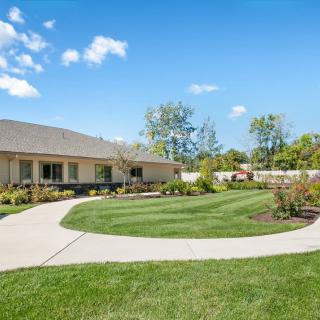 A well-maintained lawn with a winding pathway leading to a house, surrounded by trees and under a clear blue sky.