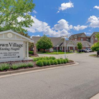Entrance to a senior living community with a sign and landscaped driveway.