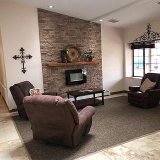 A cozy living room with recliner chairs facing a stone fireplace, decorated with wall art and a large window providing natural light.