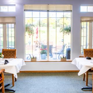A cozy dining area with tables set for guests, featuring large windows that offer an inviting view of the outdoors.