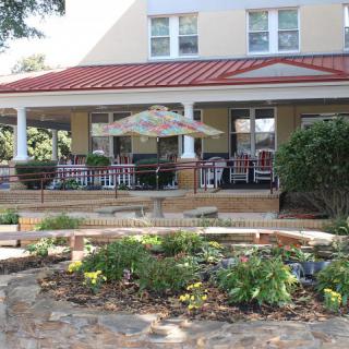 A charming house with a large porch, featuring outdoor furniture and a garden in the foreground.