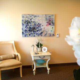 A cozy and stylish room featuring a comfortable chair, a decorative table with plants, and an abstract artwork on the wall.
