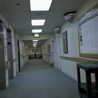A dimly lit hospital corridor with doors on either side and fluorescent lighting overhead.