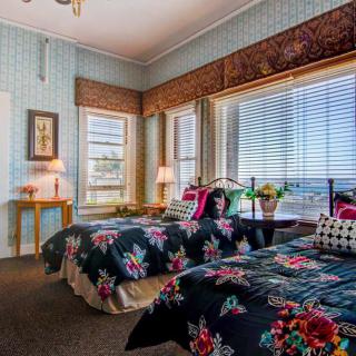 A cozy bedroom featuring twin beds with floral bedding, adorned with a large window allowing ample natural light.