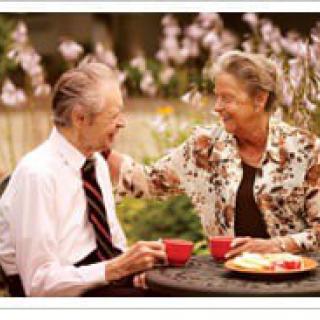 An elderly couple enjoying coffee and conversation outdoors.