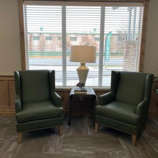 A cozy seating arrangement featuring two green armchairs and a lamp by the window.