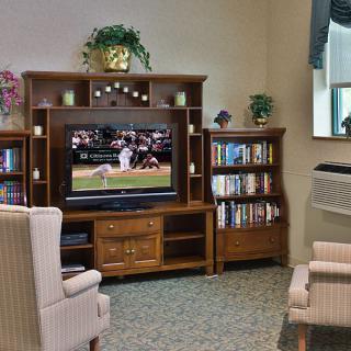 A cozy living room setup featuring a television on a wooden entertainment center, surrounded by bookshelves and comfortable seating.