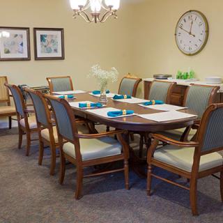 A well-decorated dining room with a large table surrounded by chairs, featuring a clock and artwork on the walls.