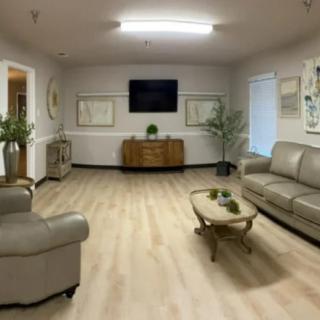 A modern living room featuring comfortable seating, a central coffee table, and a wall-mounted television, complemented by indoor plants and hardwood flooring.