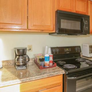 A kitchen with wooden cabinets, featuring a coffee maker, microwave, and electric stove on a granite countertop.