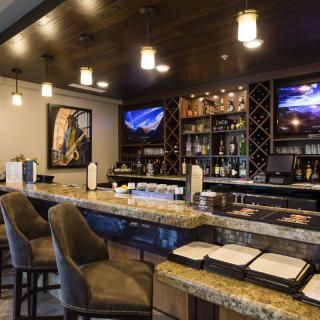 A cozy bar interior featuring a granite countertop, plush seating, and a well-stocked wine rack.