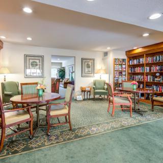 A cozy library room with tables, chairs, and bookshelves.