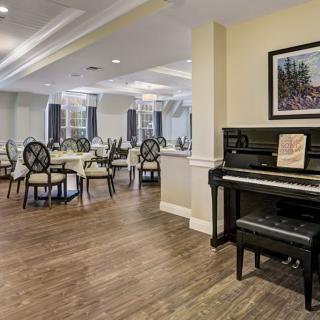 A spacious dining room with elegant seating, featuring a piano and artwork on the wall.