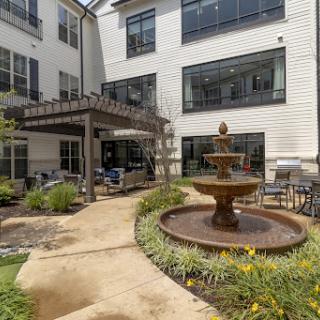 A tranquil courtyard featuring a central fountain and comfortable outdoor seating, surrounded by modern residential buildings.