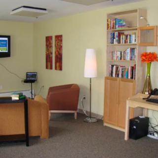 A modern office space with a desk, bookshelf, and seating area.