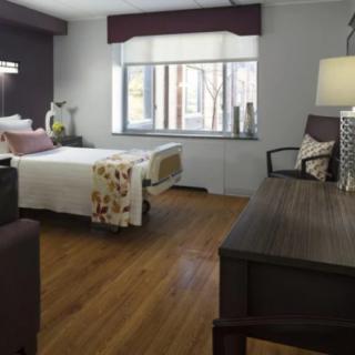 A well-lit hospital room with a bed, desk, and seating area.