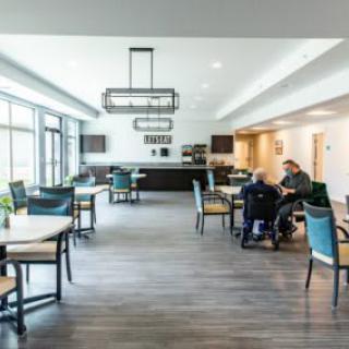 A modern dining area with several tables and chairs, featuring people interacting in a spacious, well-lit setting.