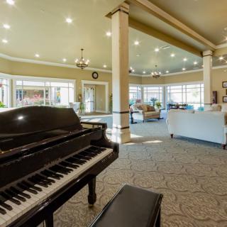 A spacious lobby interior featuring a grand piano and comfortable seating with abundant natural light.