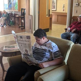 A person seated in a lobby area engrossed in reading a newspaper.