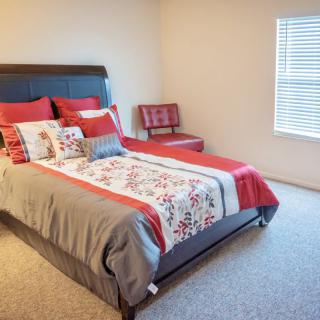 A cozy bedroom with a neatly made bed featuring red and floral accents.