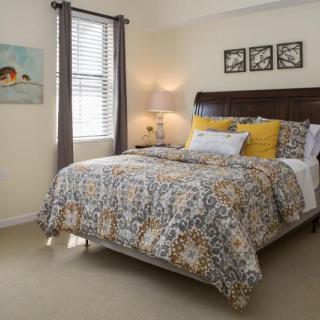 A cozy bedroom with a patterned bedspread, decorative pillows, and wall art.