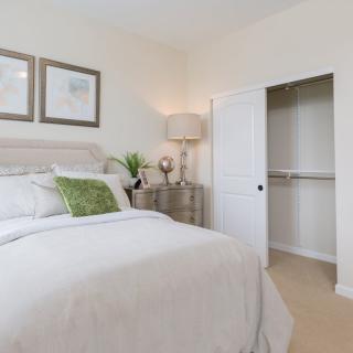 A cozy bedroom with a neatly made bed, decorative pillows, and an open closet.
