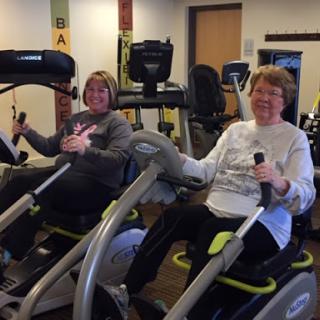 Two women enjoying a workout on elliptical machines in a gym.