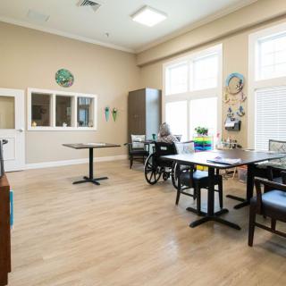 A bright dining area with tables, chairs, and a wheelchair.