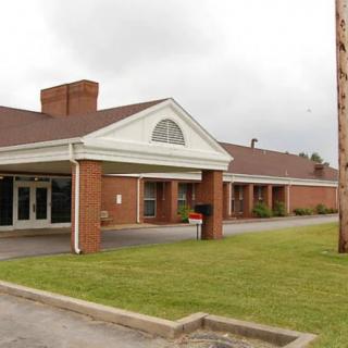 A brick building with a covered entrance and a grassy area in front.